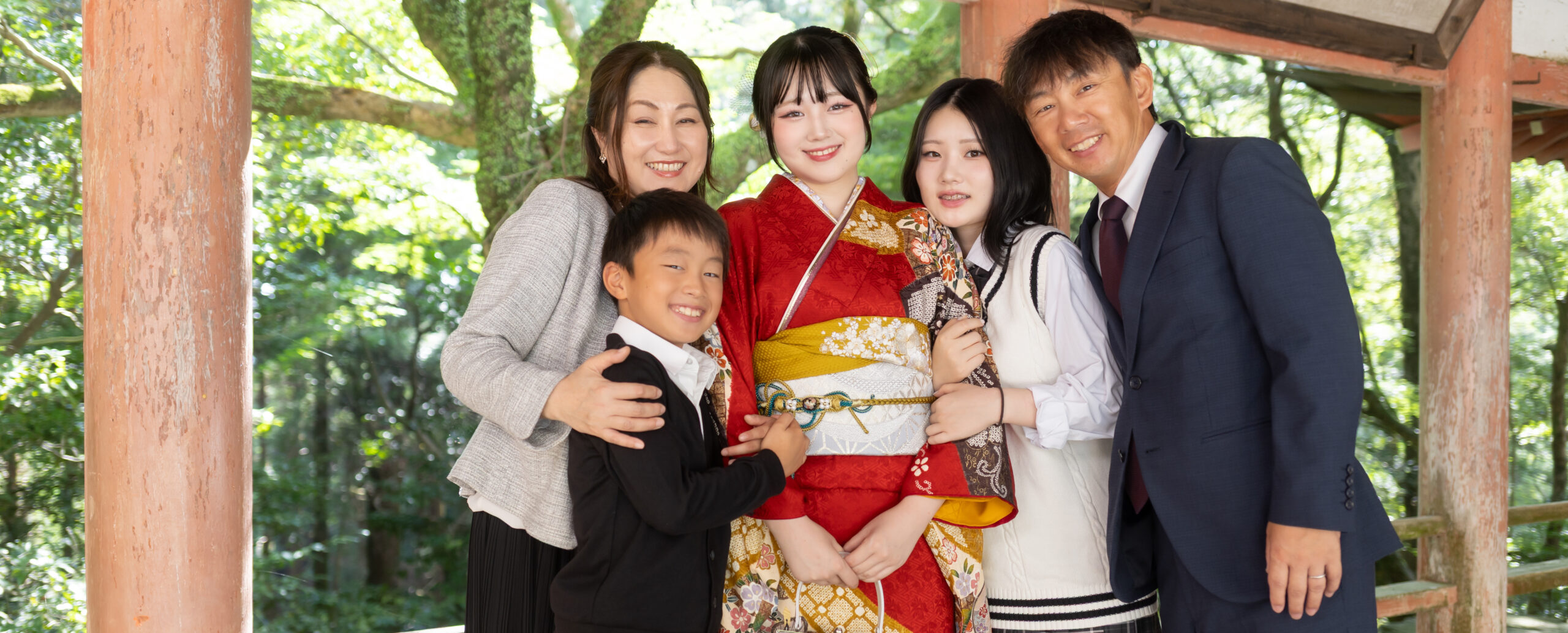 大分の柞原八幡宮で撮影した成人式の家族写真。赤い振袖姿の新成人を中心に、両親やきょうだいと笑顔で寄り添う成人記念のロケーションフォト。