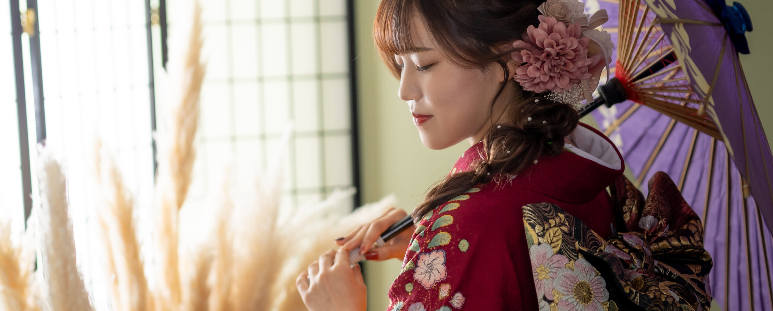 大分のPhotostudio PASSIONで、赤い振袖に紫の和傘を合わせ、ピンクの花飾りと編み下ろしヘアが映える横顔を撮影した成人式前撮り写真