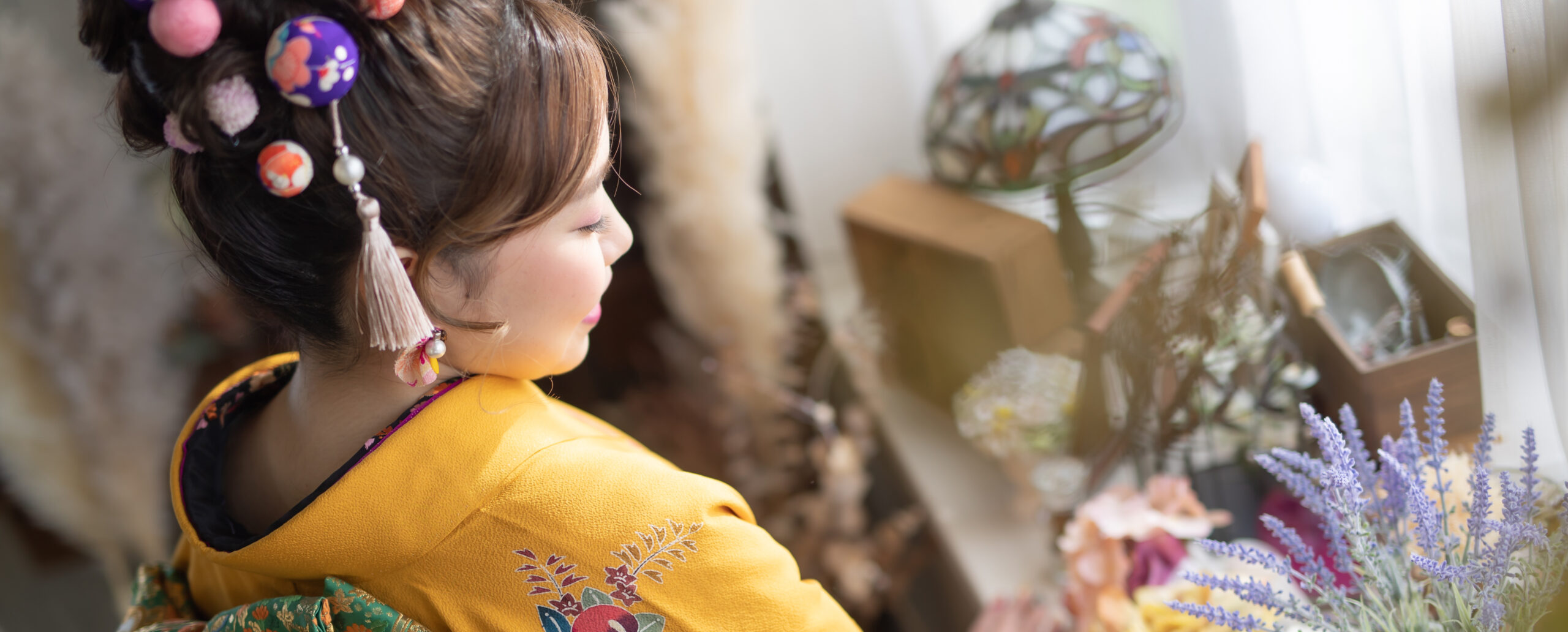 大分のPhotostudio PASSIONで、黄色の振袖に色鮮やかな玉かんざしを合わせ、窓辺で横顔と華やかな髪飾りを撮影した成人式前撮り写真