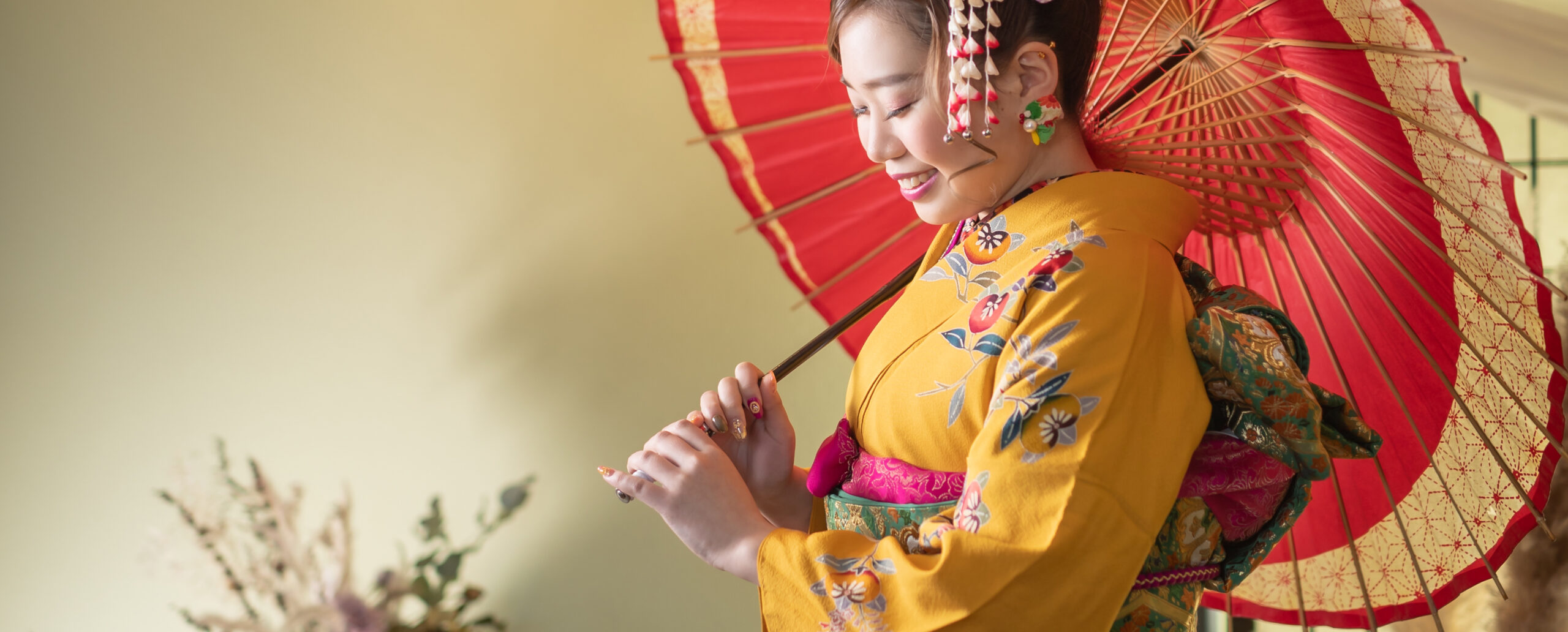 大分のPhotostudio PASSIONで、黄色の花柄振袖に華やかな髪飾りを合わせ、赤い和傘を手に微笑む成人式前撮りのスタジオ写真