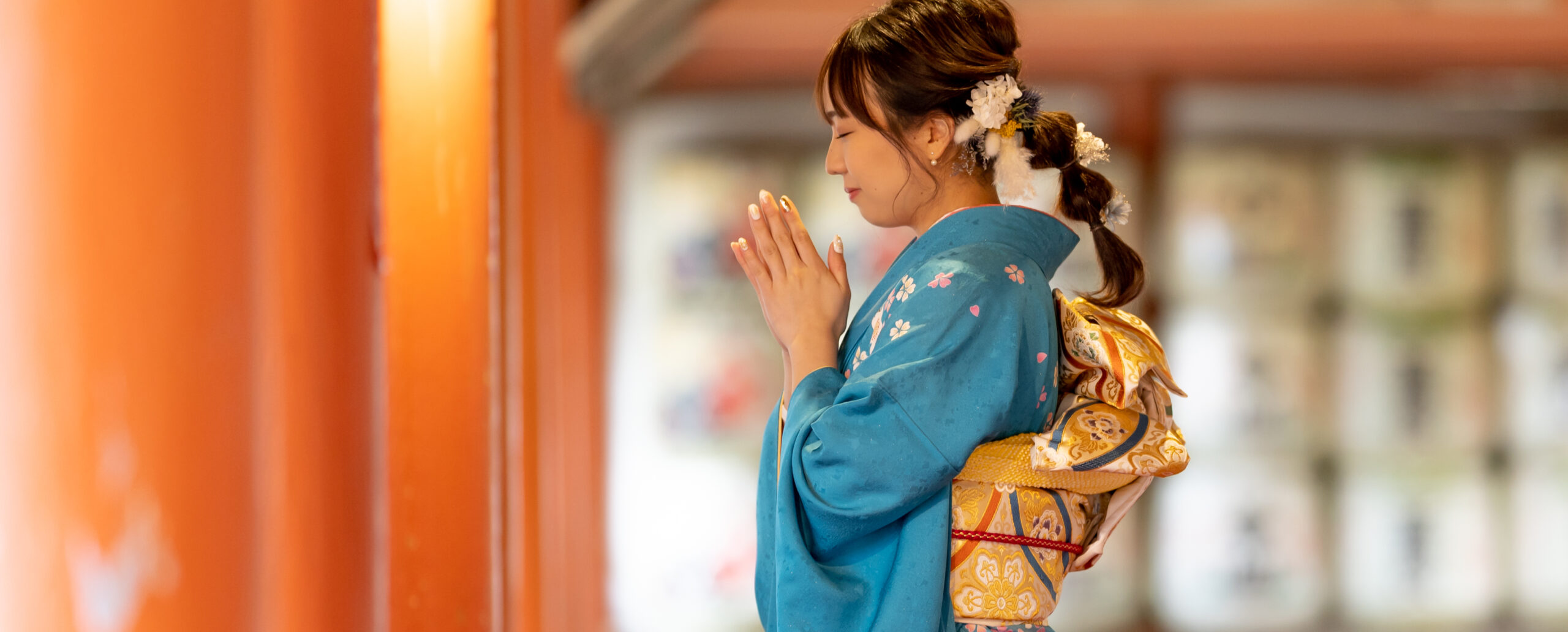 大分の柞原八幡宮で、青緑色の振袖と金色の帯を身にまとい、目を閉じて手を合わせる女性の成人式前撮りロケーション写真